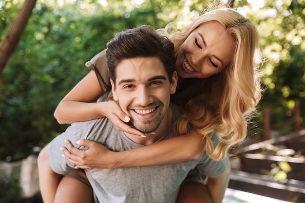 Cheerful young man carrying his pretty girlfriend on his back