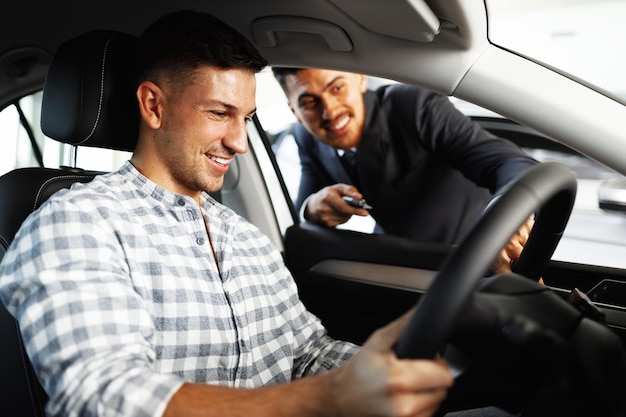 Cheerful young man customer buys a new car in a dealership