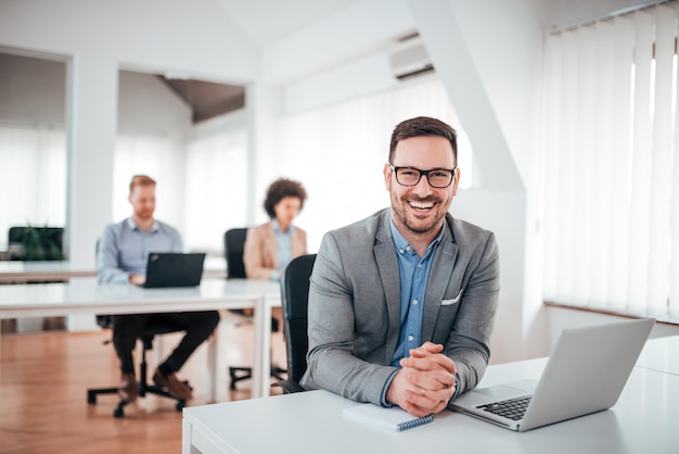 Cheerful young man sitting in office with laptop.