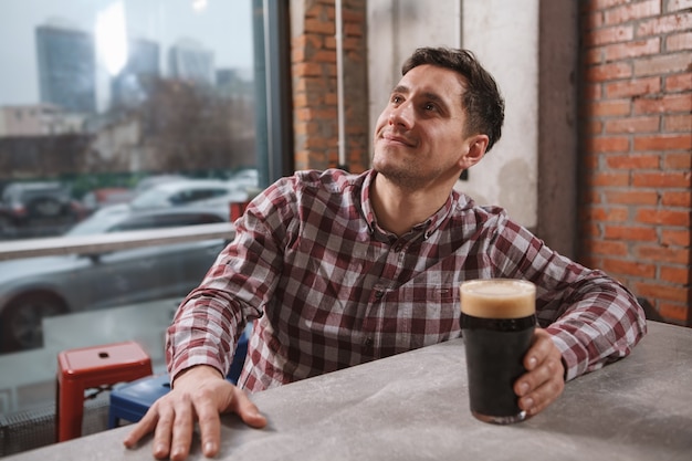 Cheerful young man smiling, watching tv at beer pub, copy space