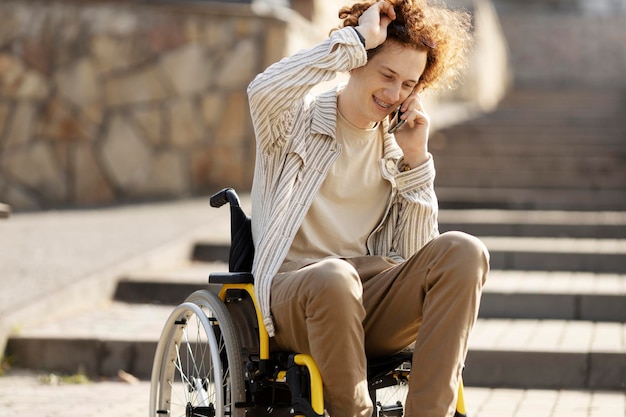 Cheerful young man in a wheelchair talking on the phone Smiling guy in the park