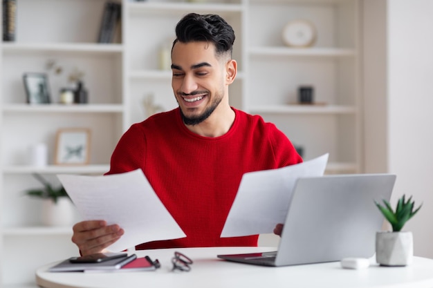 Cheerful young middle eastern man manager with beard works with documents at workplace with computer