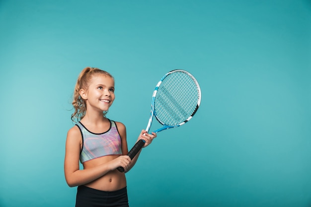 Cheerful young sports girl playing tennis isolated over blue wall