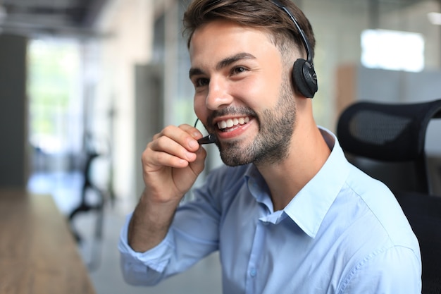 Cheerful young support phone male operator in headset, at workplace while using laptop, help service and client consulting call center concept.