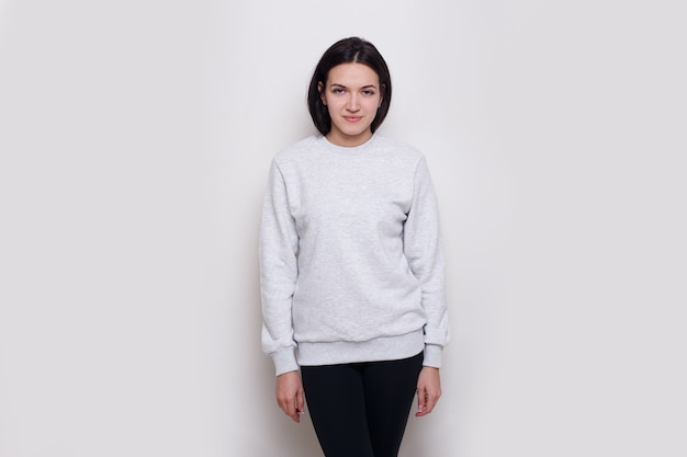 Cheerful young woman brunette in a light grey sweater, isolated on white background. Space for text.