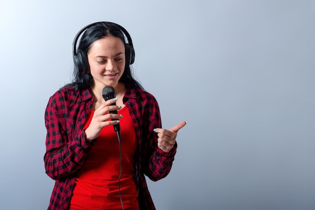 Cheerful young woman in casual clothes with headphones sing song in microphone mock up copy space