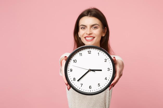 Cheerful young woman in casual light clothes posing isolated on pastel pink wall background, studio portrait. People sincere emotions lifestyle concept. Mock up copy space. Holding in hands clock.