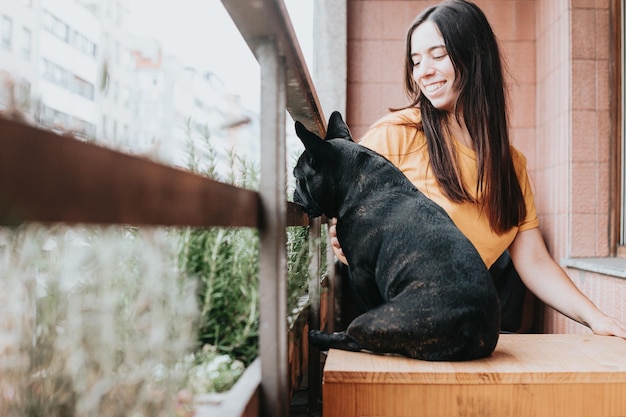 Cheerful young woman cuddling and taking care of her french bulldog on homePuppy observing concentrated looking the cityPlayfulhumorous and cheerful friendship partner Cozy domestic atmosphere