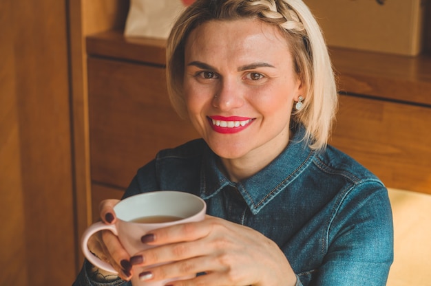 Cheerful young woman drinking warm coffee or tea enjoying it while sitting in cafe. Attractive woman holding a cup of coffee.. Warming drink.