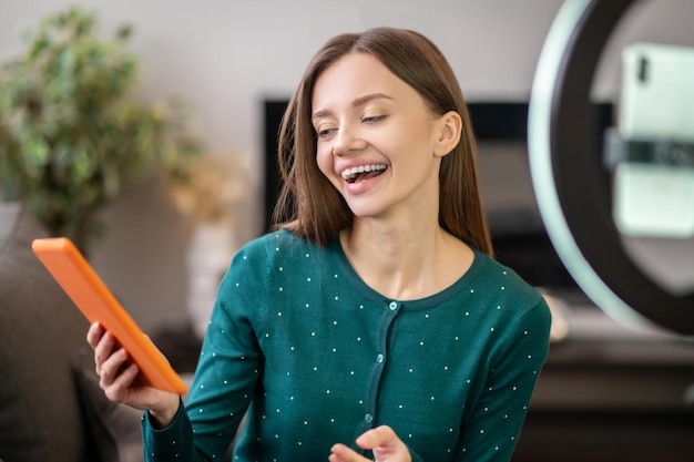 Cheerful young woman in green shirt in front of camera making online workshop