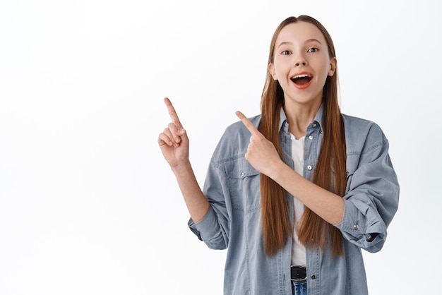 Cheerful young woman laughing pointing aside at logo showing banner on copyspace upper left corner demonstrate promotional text standing against white background