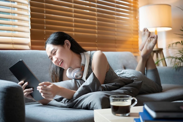 Cheerful young woman lying on couch and using digital tablet