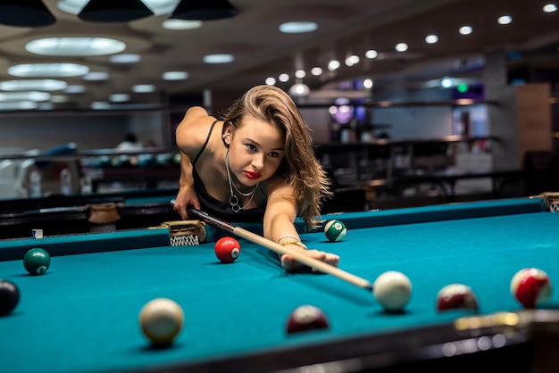 Cheerful young woman playing billiard in pub