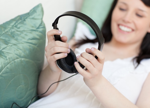 Cheerful young woman putting headphones lying on a sofa 