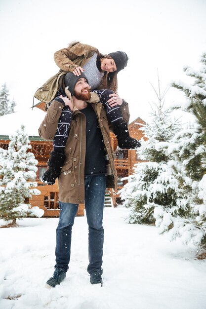 Cheerful young woman sitting on man shoulders and laughing in winter