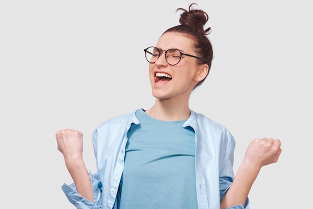 Cheerful young woman smiling wide open mouth dressing in blue shirt wearing round eyeglasses isolated over white background People and emotions concept