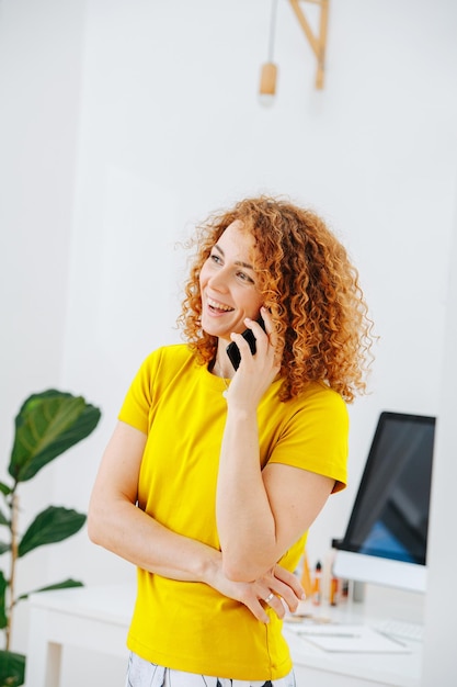 Cheerful young woman speaking on her phone standing in front of her workplace