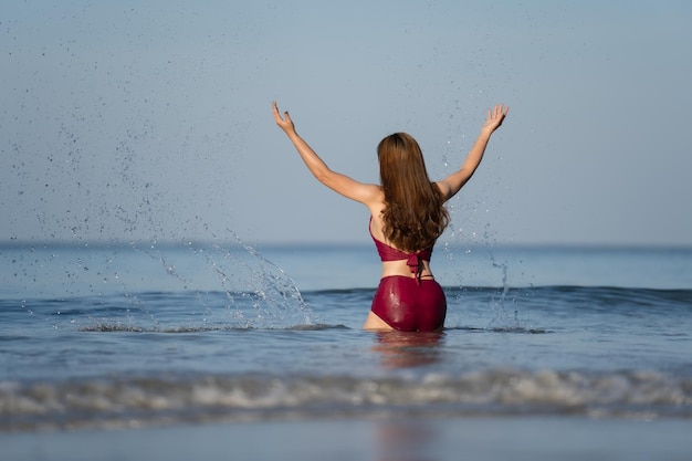 Cheerful young woman in swimsuit playing water splashing on the sea beach at Koh Chang island Thailand