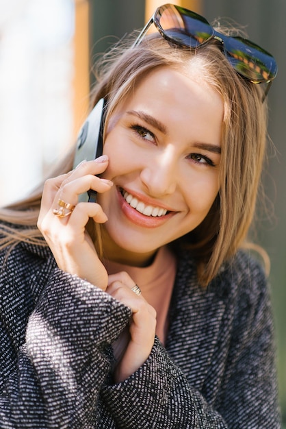 Cheerful young woman talking on a mobile phone while standing inside a cafe during the day