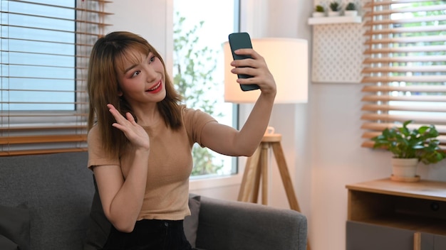 Cheerful young woman waving hand chatting online making video call on her smart phone