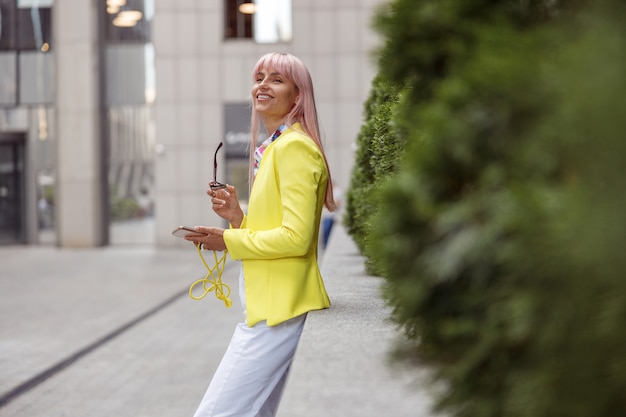 Cheerful young woman with cellphone standing on the street