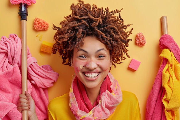 Photo cheerful young woman with cleaning product on face posing with mop amidst