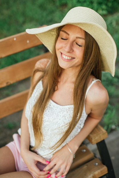 Cheerful young woman with closed eyes on bench at park