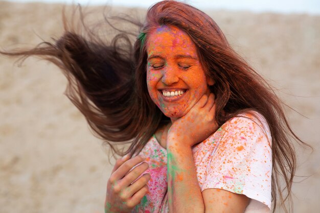 Cheerful young woman with wind in hair celebrating Holi colors festival at the desert. Space for text