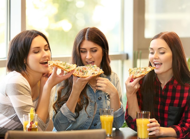 Cheerful young women eating tasty pizza in cafe