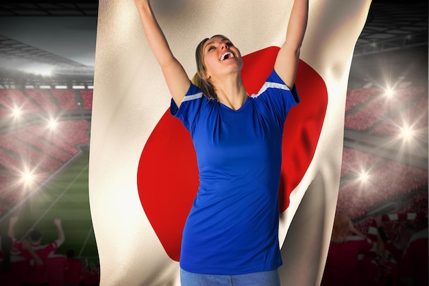 Cheering football fan in blue jersey holding japan flag against vast football stadium with fans in red