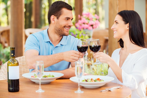 Cheers! Beautiful young loving couple toasting with red wine and smiling while relaxing in outdoors restaurant together