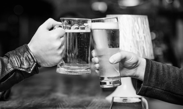 Cheers concept Glass with fresh lager draft beer with foam Male hands hold mugs filled with cold tasty beer in bar Friday leisure tradition Beer mugs at bar counter defocused background