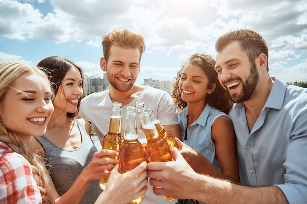 Cheers to friends group of happy young people are clinking bottles with beer and smiling