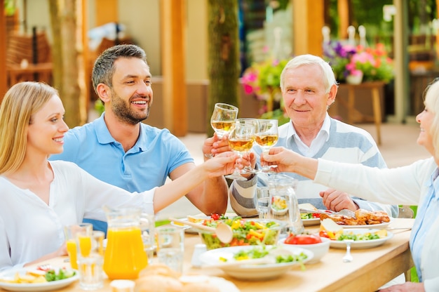 Cheers to the nearest! Happy young and senior couples sitting at the dining table and toasting with wine