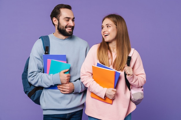 a cheery loving couple friends students isolated over purple wall holding books.