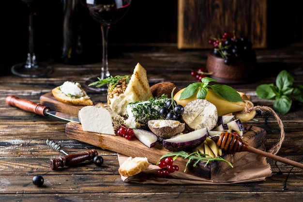 Photo cheese appetizer selection. red currant, honey, basil, grapes and nuts on rustic wooden board