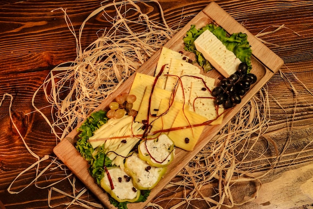 Cheese assortment in wooden tray with grapes decorated with dried grass