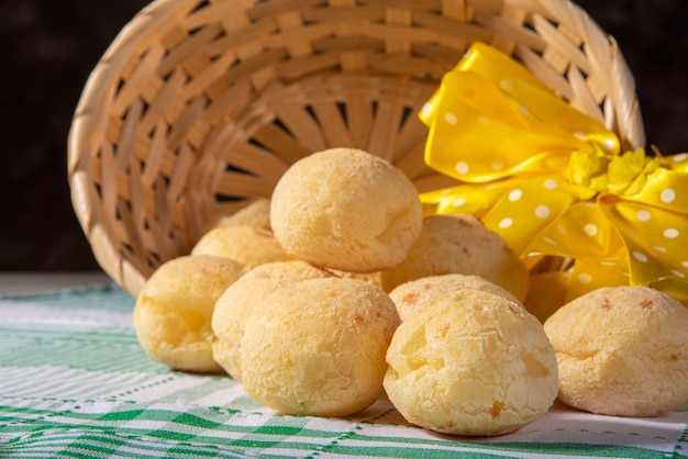 Cheese bread, straw basket with a bow of yellow ribbon fallen with cheese bread on a checkered tablecloth.