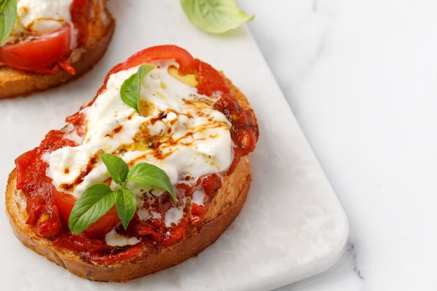 Cheese Bruschettas with stracciatella tomatoes basil on marble board marble background copy space