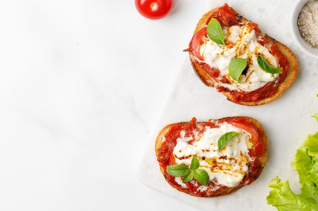 Cheese Bruschettas with stracciatella tomatoes basil on marble board top view copy space