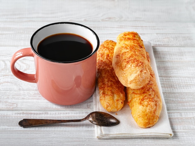 Cheese buns, bread with cheese and a cup of coffee with a spoon on a white wooden background