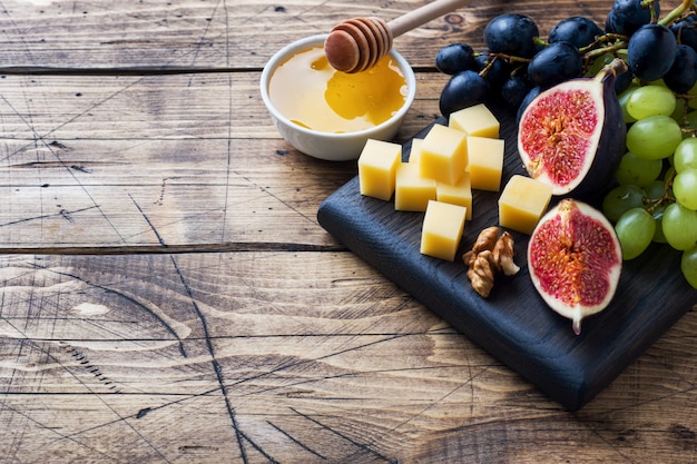 Photo cheese cubes, fresh fruit figs grapes honey walnut on wooden chopping board. copyspace.