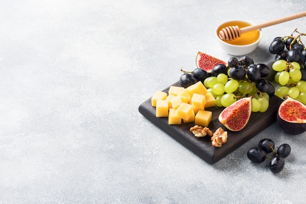 Cheese cubes, fresh fruit figs grapes Honey walnut on wooden chopping Board. copyspace.