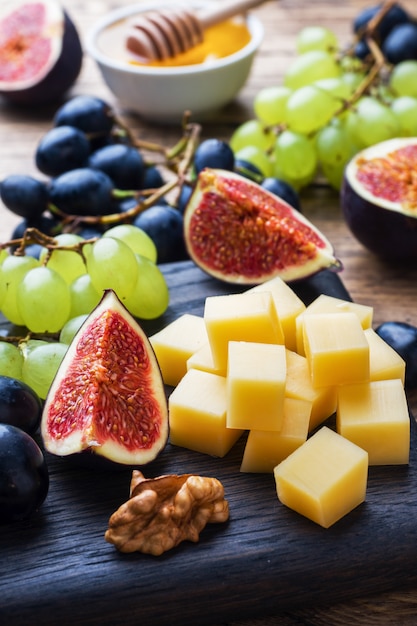 Cheese cubes, fresh fruit figs grapes Honey walnut on wooden chopping Board. Selective focus. Close up.