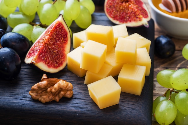 Cheese cubes, fresh fruit figs grapes Honey walnut on wooden chopping Board. Selective focus. Close up.