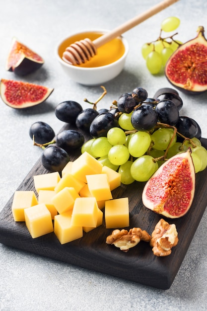 Cheese cubes, fresh fruit figs grapes Honey walnut on wooden chopping Board. Selective focus. Close up.