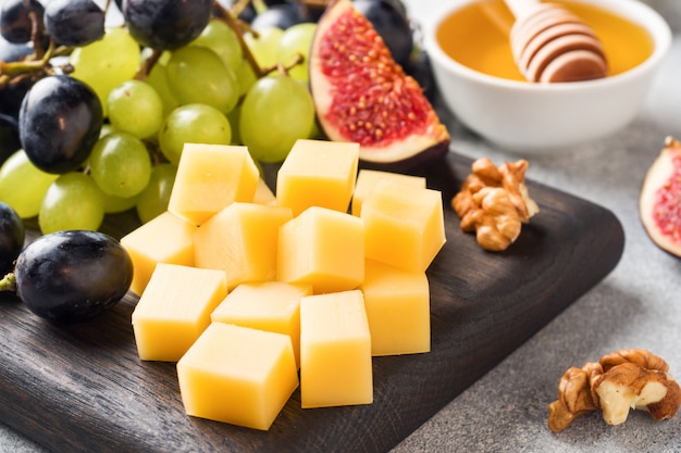 Cheese cubes, fresh fruit figs grapes Honey walnut on wooden chopping Board. Selective focus. Close up.