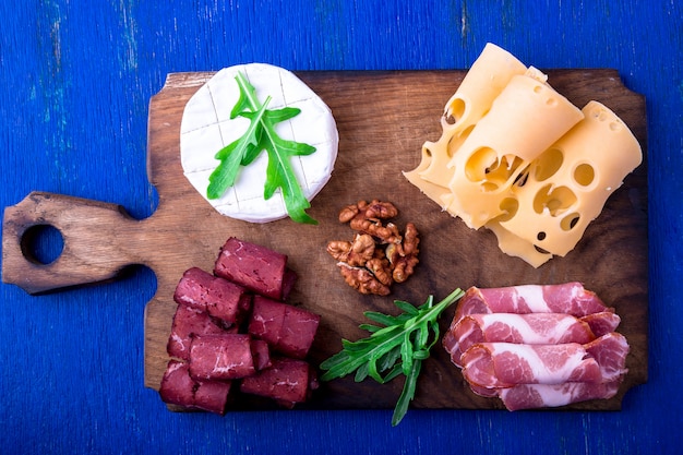 Cheese and meat plate with walnuts on blue wooden surface,