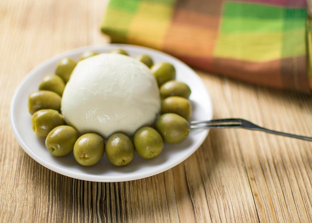 Cheese mozzarella and olives on a plate on a wooden background