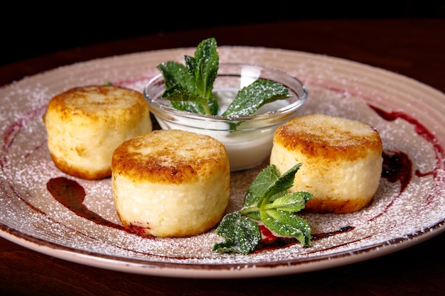 Cheese pancake, cheesecakes with sour cream, jam, and mint on a plate. Morning breakfast.